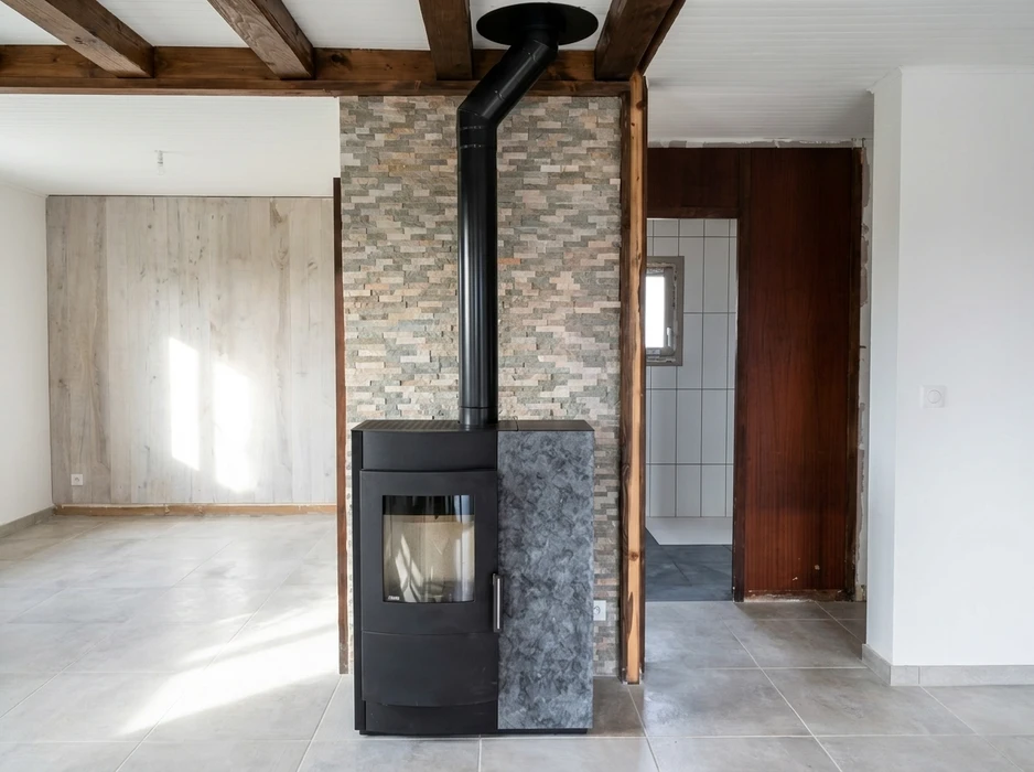 Intérieur rénové avec poêle à bois noir sur socle en pierre naturelle grise, adossé à un mur en pierre de parement multicolore
